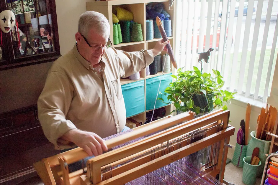 Michael Daitch weaving at a loom in a cozy room