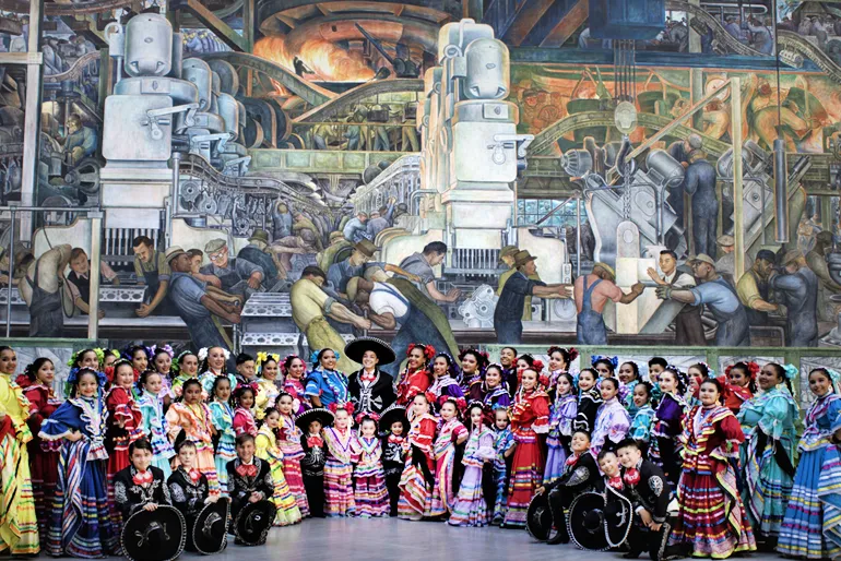 Members of Ballet Folklorico de Detroit posing together in front of the DIA's Detroit Industry Murals