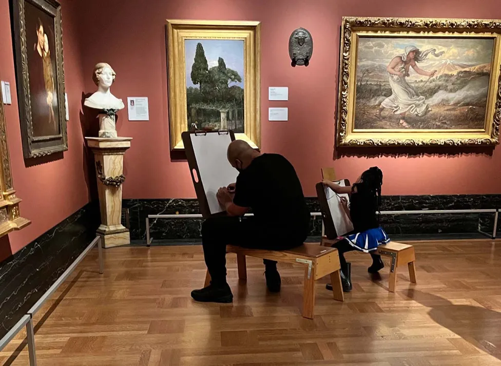 An adult and a young child sit together on separate easel stools