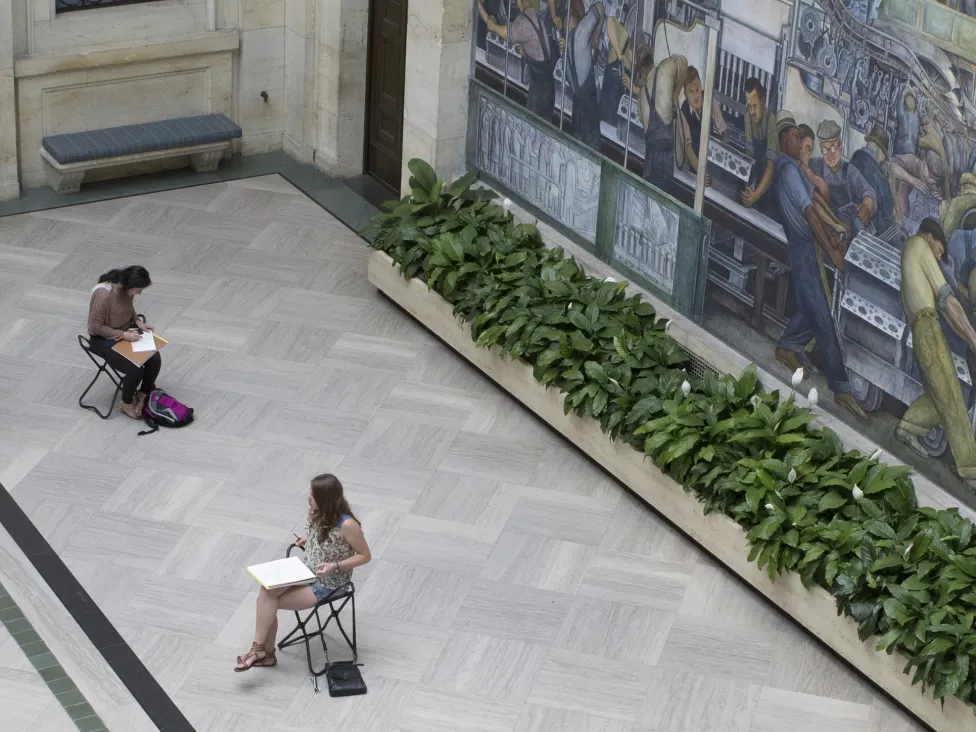 Two patrons sitting on stools and drawing in the DIA's Rivera Court