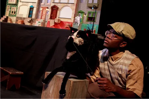 A boy operates a black and white cat puppet