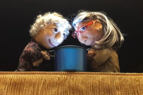 Two puppets hang their heads over a camping mug.