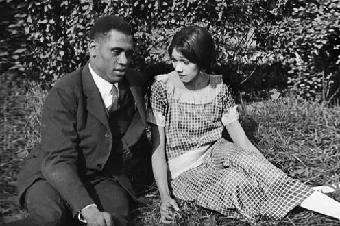 A man and a woman sit on the grass together in nice clothes.
