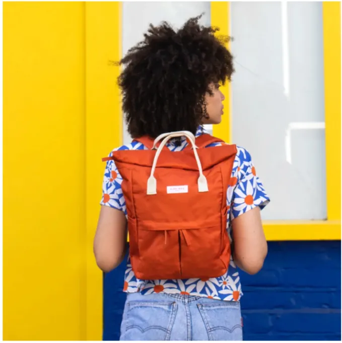 A woman with a short afro faces away from the camera, showcasing her large orange backpack.