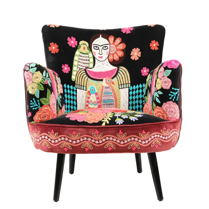 A chair with embroidery featuring flowers and a depiction of Frida Kahlo with a parrot